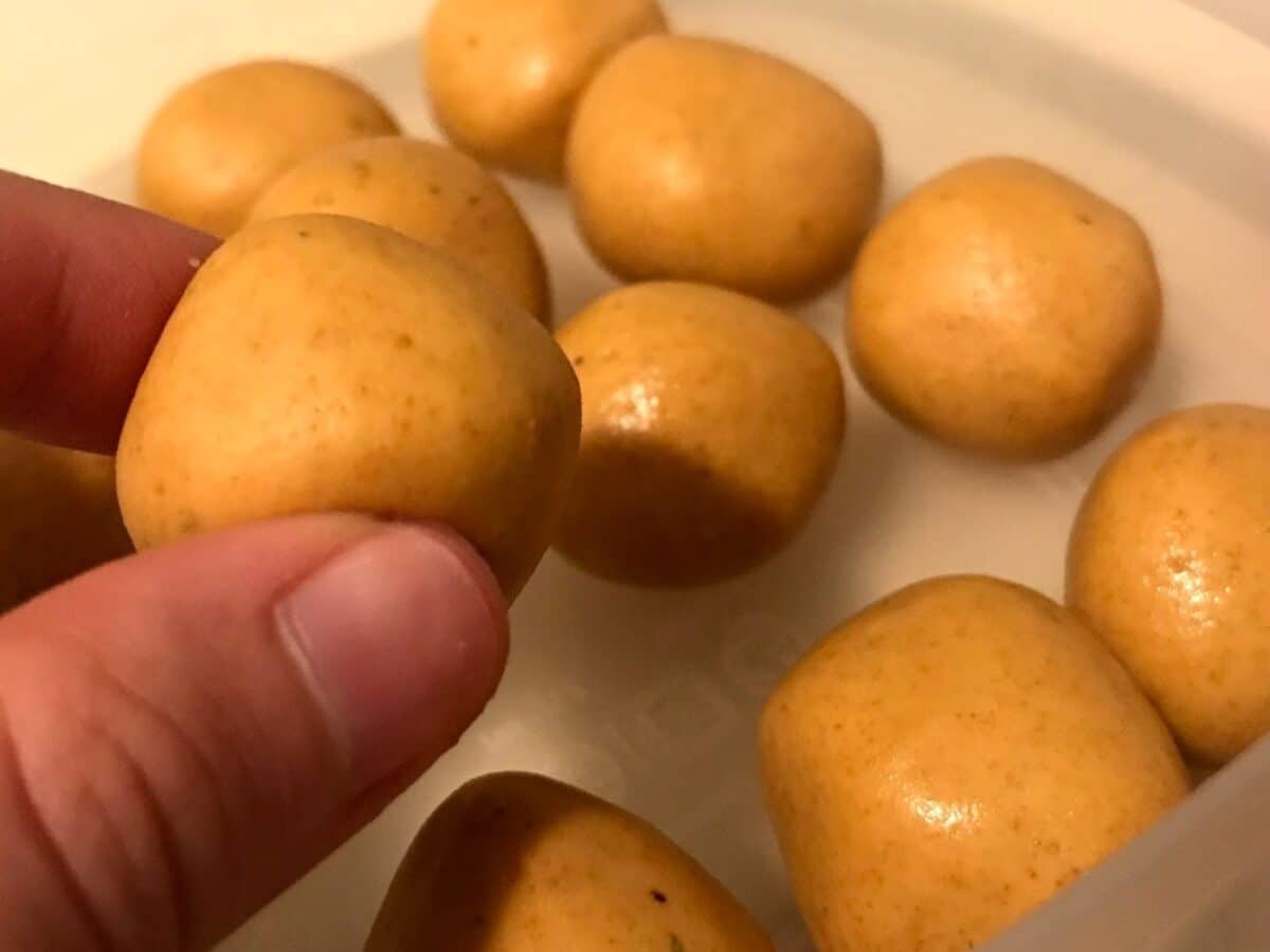 a hand holds up a small vegan besan ladoo.