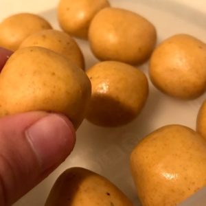 a hand holds up a small vegan besan ladoo.