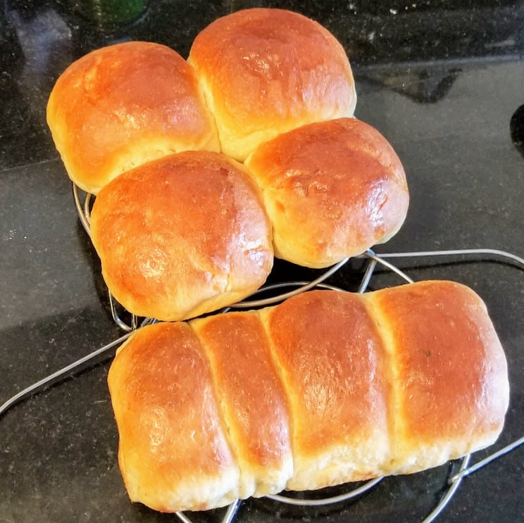 homemade hokkaido milk bread buns and loaf on a cooling rack over a granite countertop.