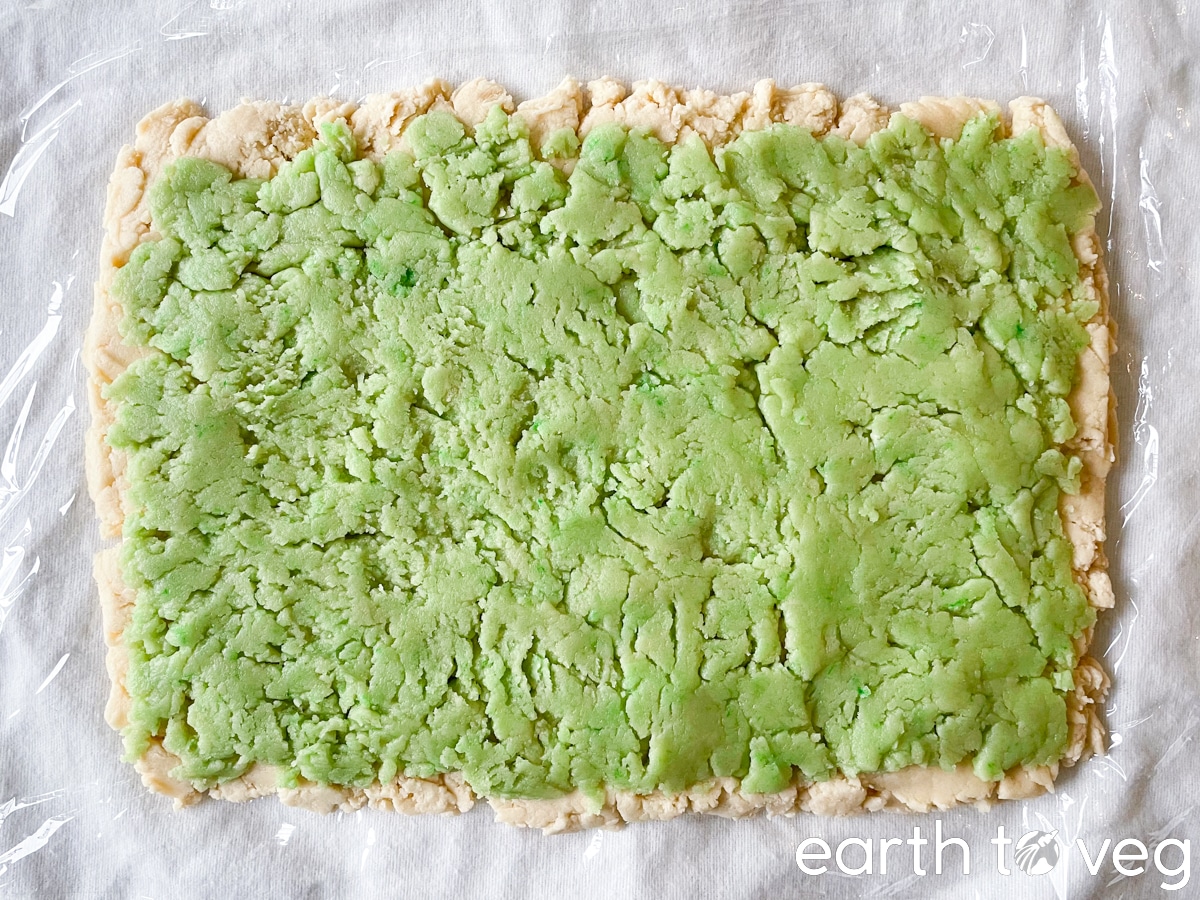 A green layer of cookie dough is placed over the base layer of white cookie dough.