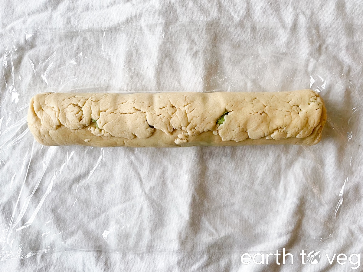 A rolled up cookie dough log on a white tablecloth.