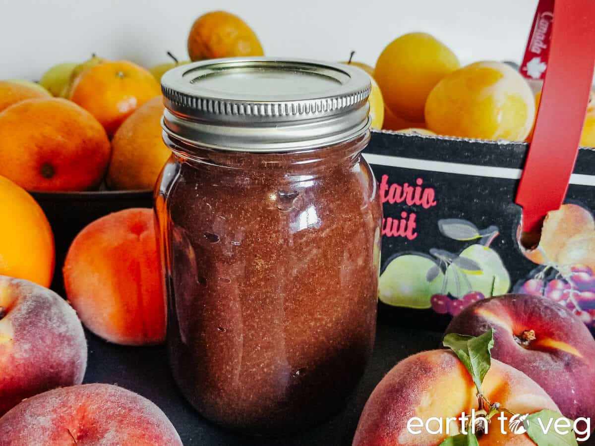 A mason jar full of rhubarb butter surrounded by fresh summer fruit.