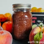 A glass pint jar of rhubarb butter next to some summer stonefruit.