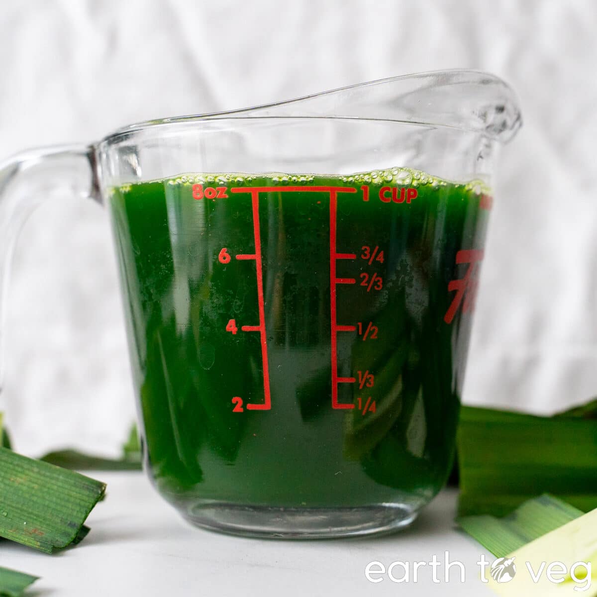 Freshly blended and strained pandan juice in a Pyrex cup on a white countertop.