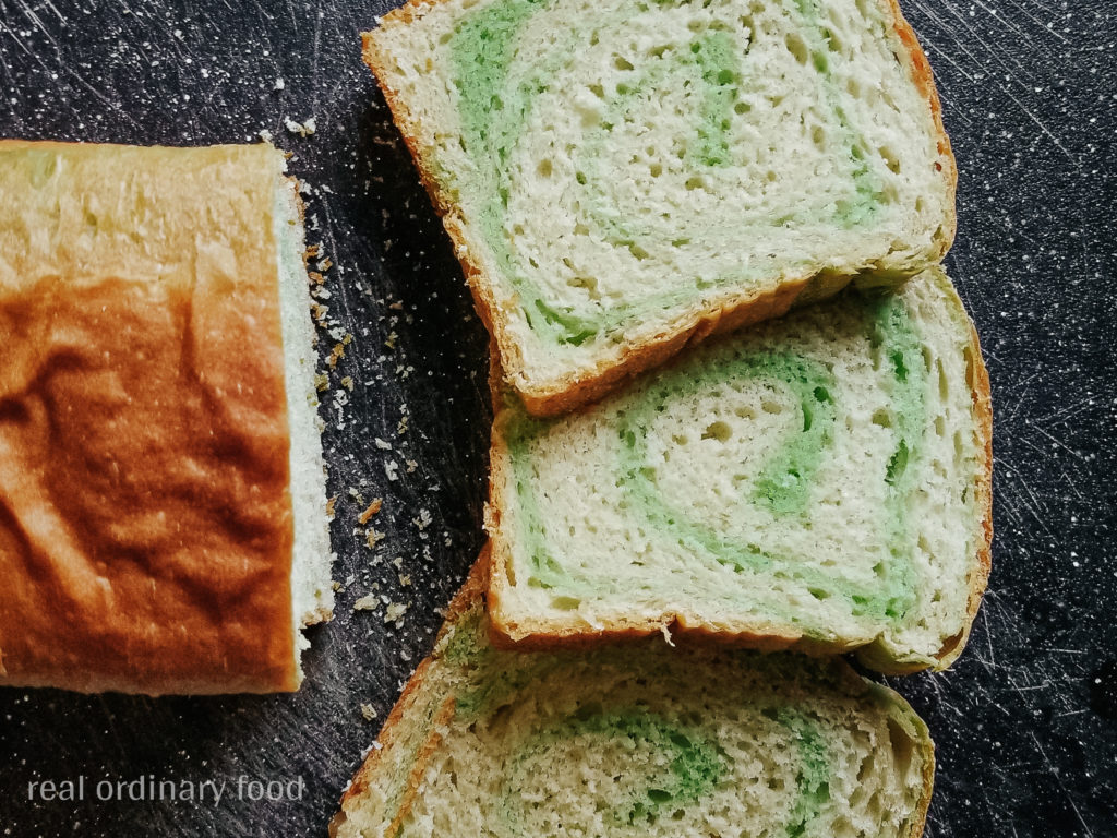 Three slices of vegan pandan swirl bread laid out on a black cutting board.
