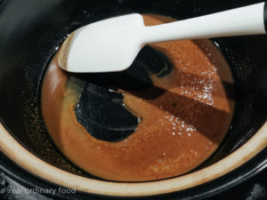 Dark vegan gumbo roux is stirred around by a white spatula in a black Dutch oven.