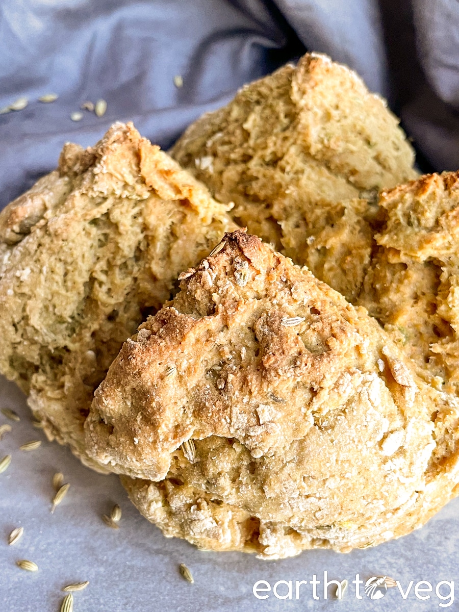 a boule of whole wheat soda bread on a grey tile backdrop with scattered fennel seeds