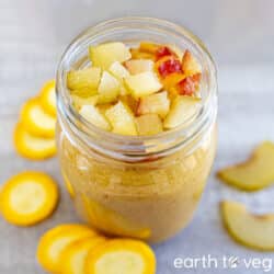 Yellow zucchini smoothie in a glass mason jar on a grey countertop, surrounded by zucchini and peach slices.