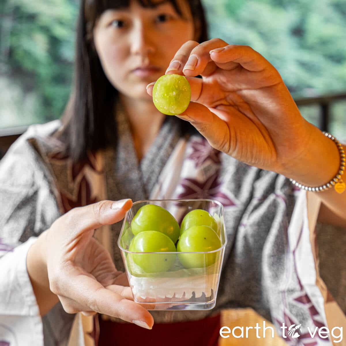 A young woman in a yukata holds up a shine muscat grape bit in half.
