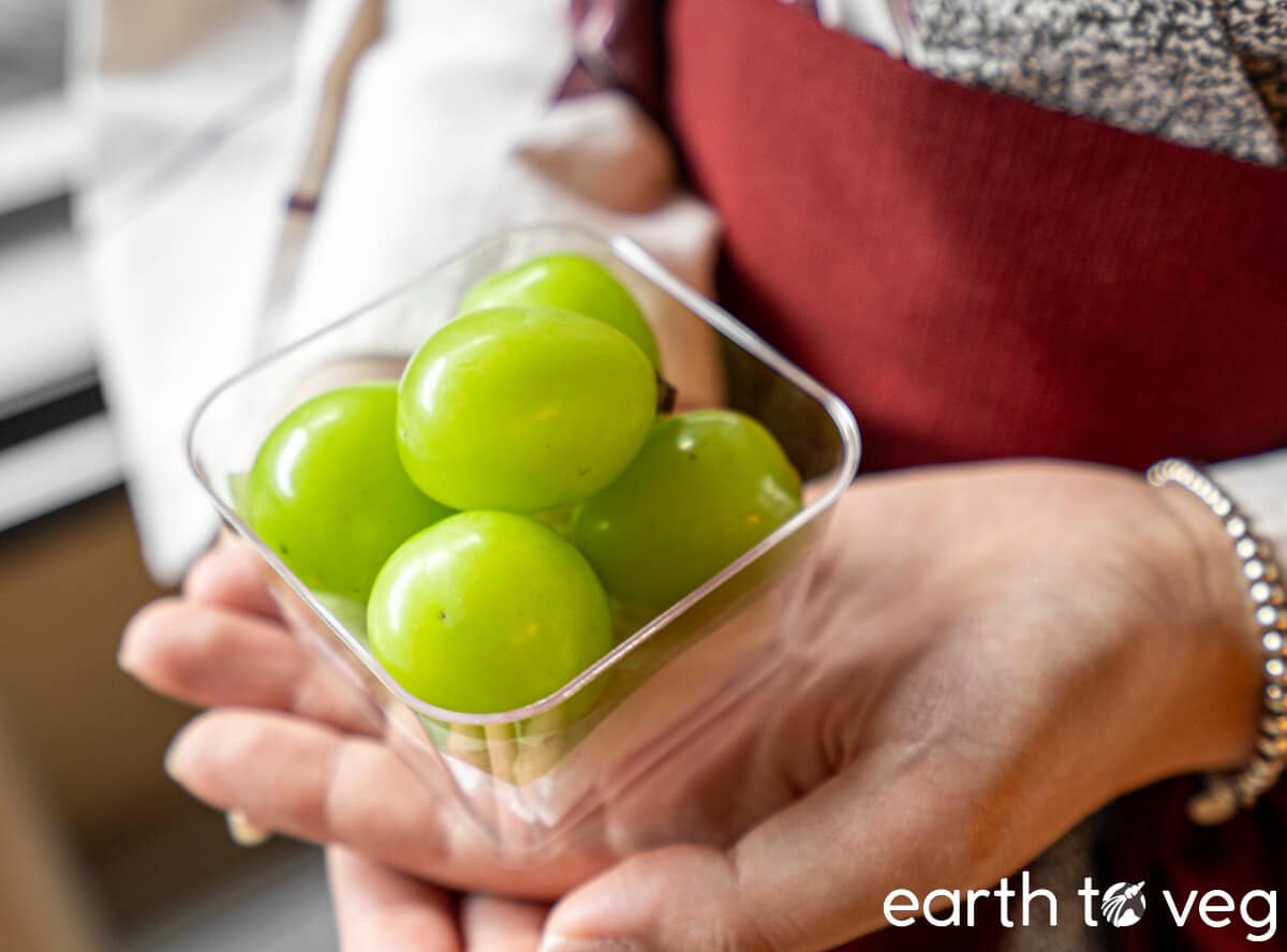 Five shine muscat grapes in a small plastic punnet held in a woman's hands.