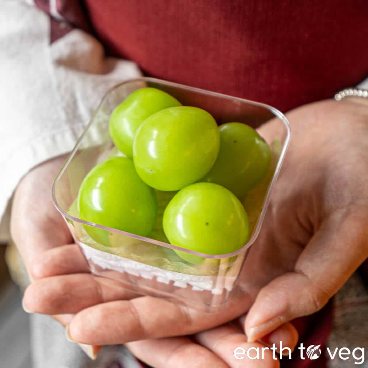 Hands hold up a small container of Japanese shine muscat grapes.