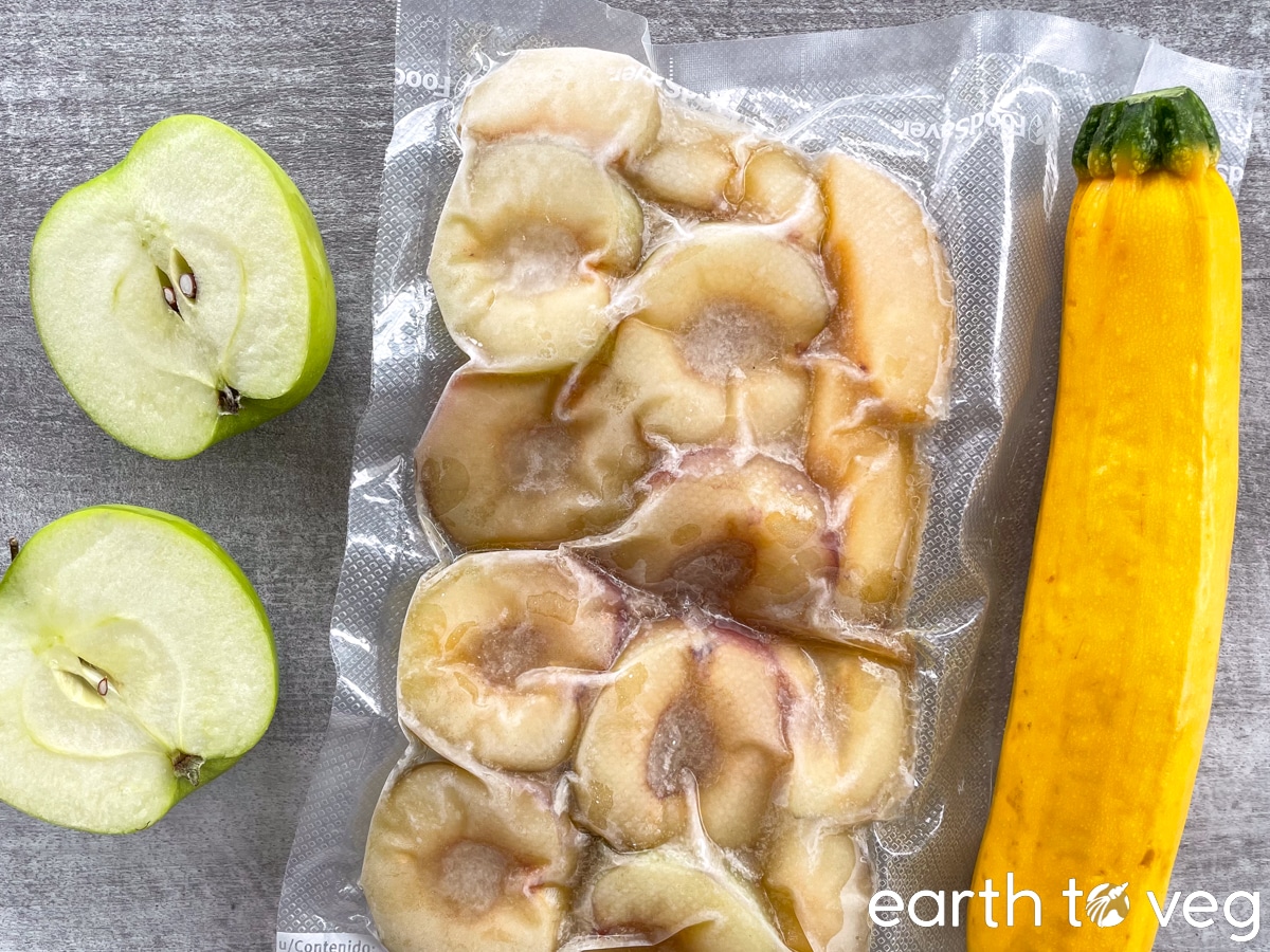 Topdown view of granny smith apples, yellow zucchini, and frozen sierra honey plums on a grey countertop.