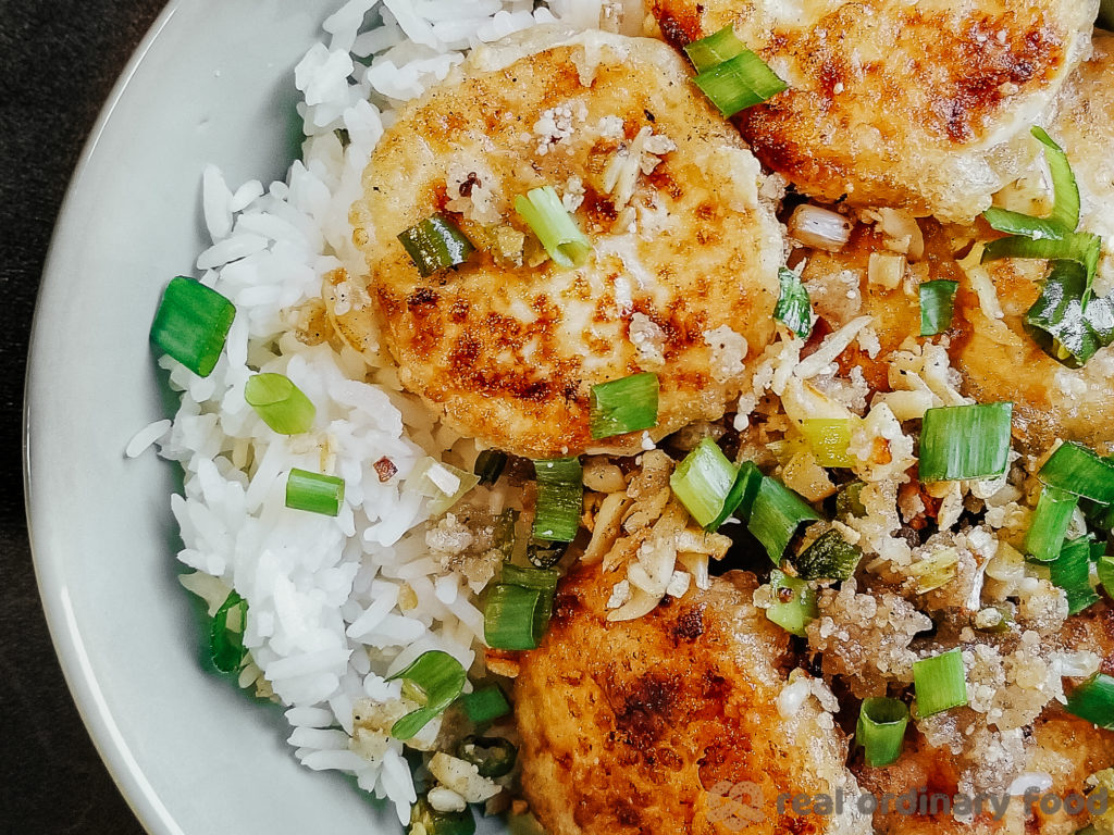 A bowl of crunchy pan-fried tofu served with scallions over steamed rice.