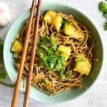 A pair of wooden chopsticks over a green bowl filled with cucumber bean curd salad.