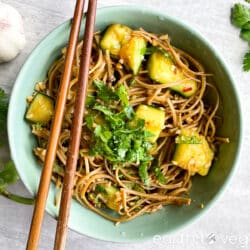 A pair of wooden chopsticks over a green bowl filled with cucumber bean curd salad.
