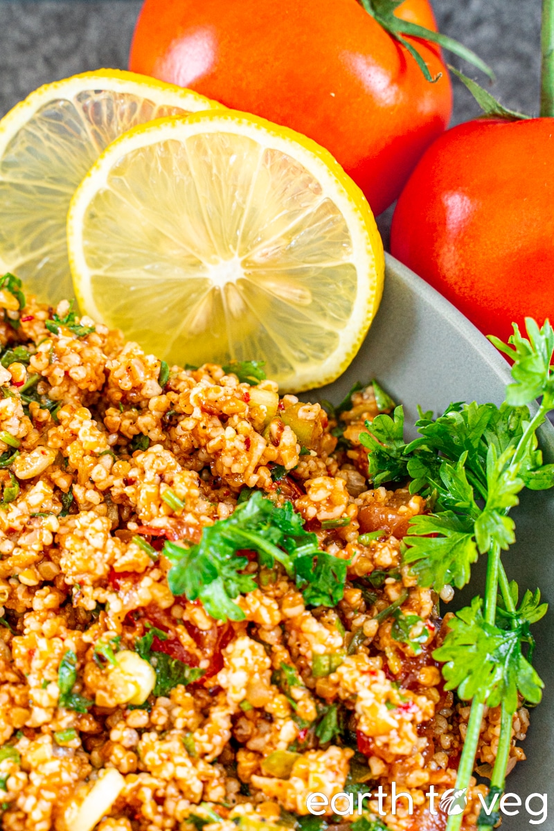 Closeup of kısır salad with parsley, lemon slices, and tomatoes in the background.