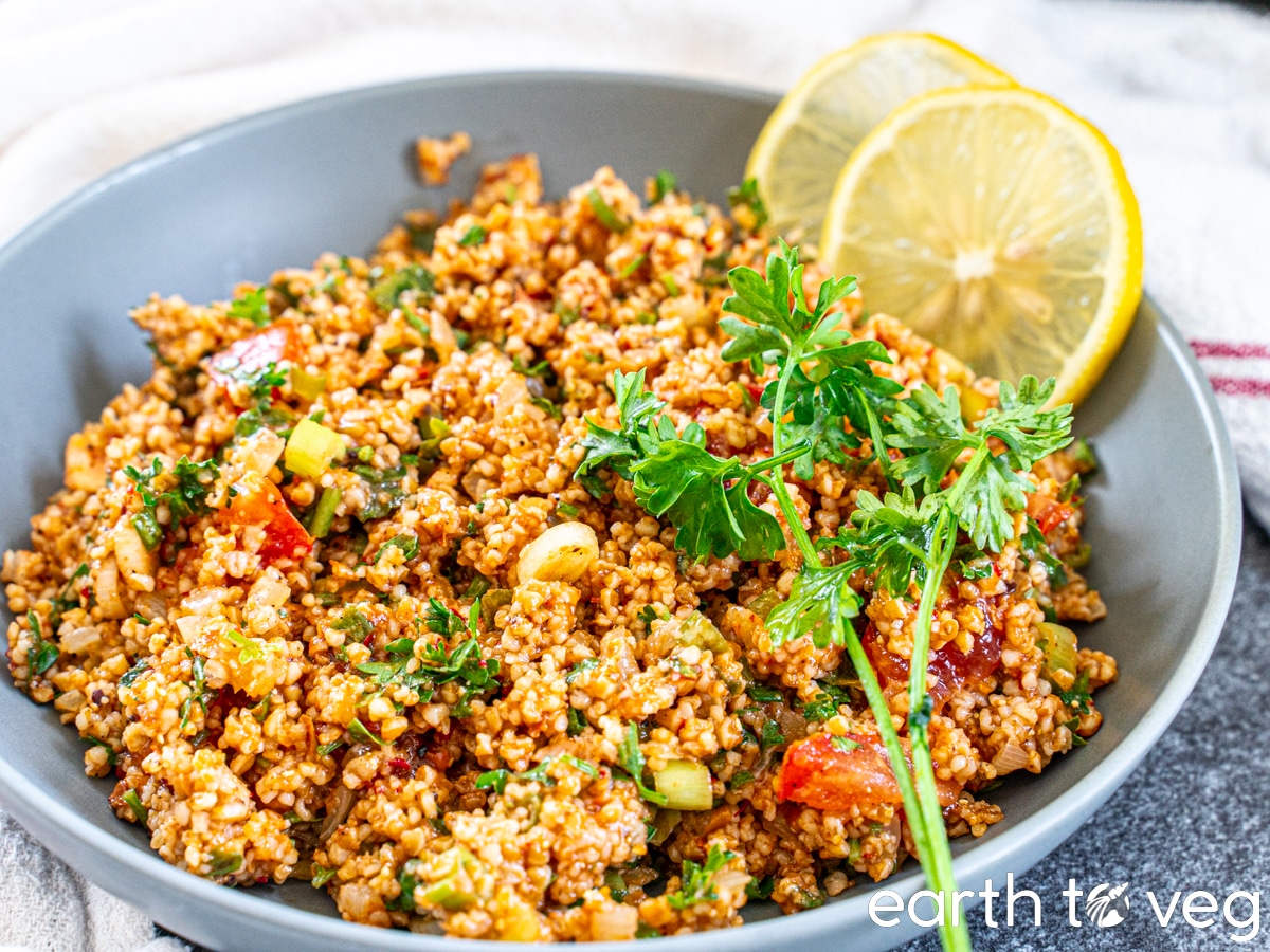 Turkish kısır salad made with dalia (cracked wheat), in a grey bowl nestled with a white tea towel.