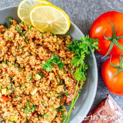 A grey bowl filled with kisir salad is garnished with parsley sprigs, lemon slices, and tomatoes.