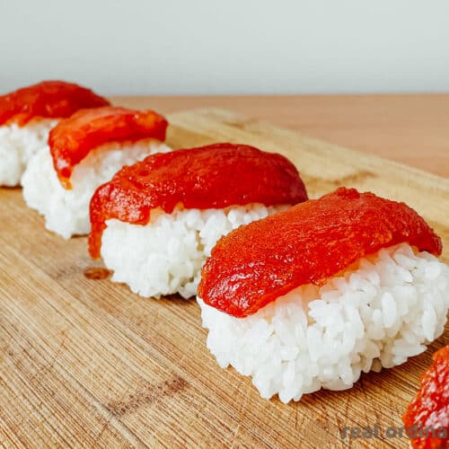 Marinated tomato nigiri sushi on a wooden cutting board.