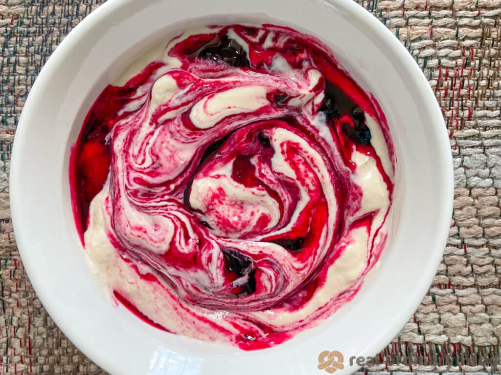 Haskap jam swirled through homemade vegan yogurt in a white Corningware bowl.