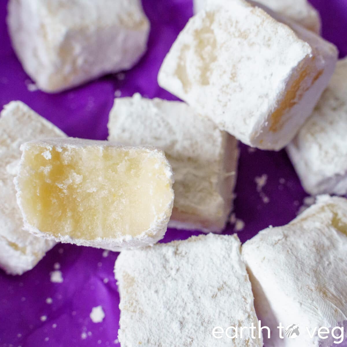 A pile of small square mung bean okara paste cakes on a purple backdrop.
