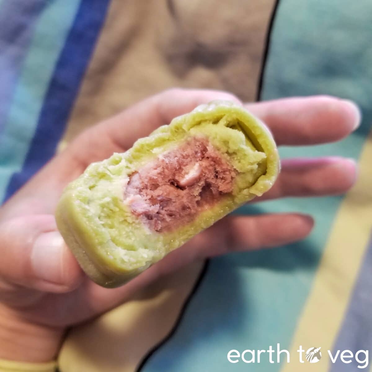 A hand holds up a green matcha snow skin mooncake with red bean paste.