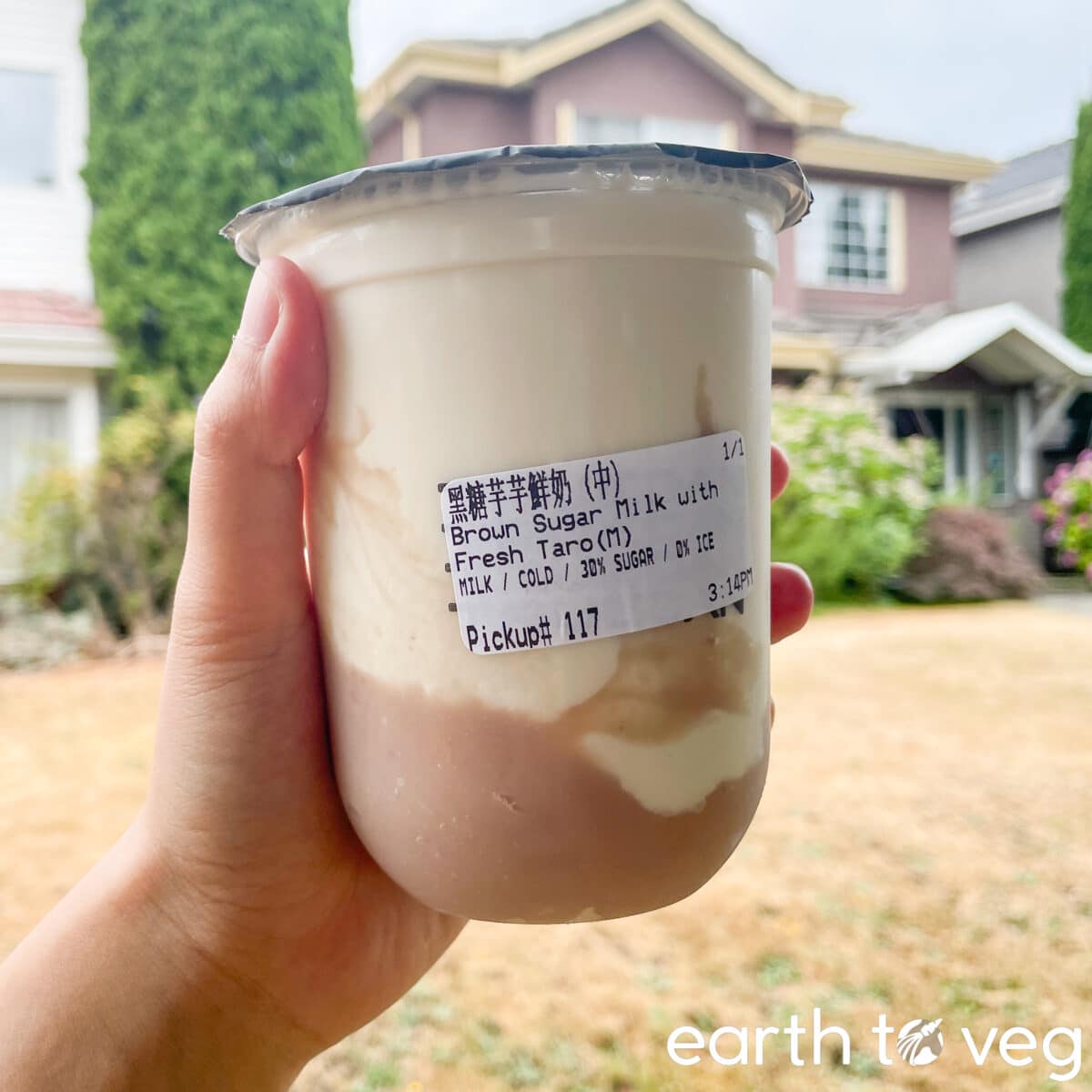 A hand holding up a cup of taro milk purchased from Jenjudan (Truedan).