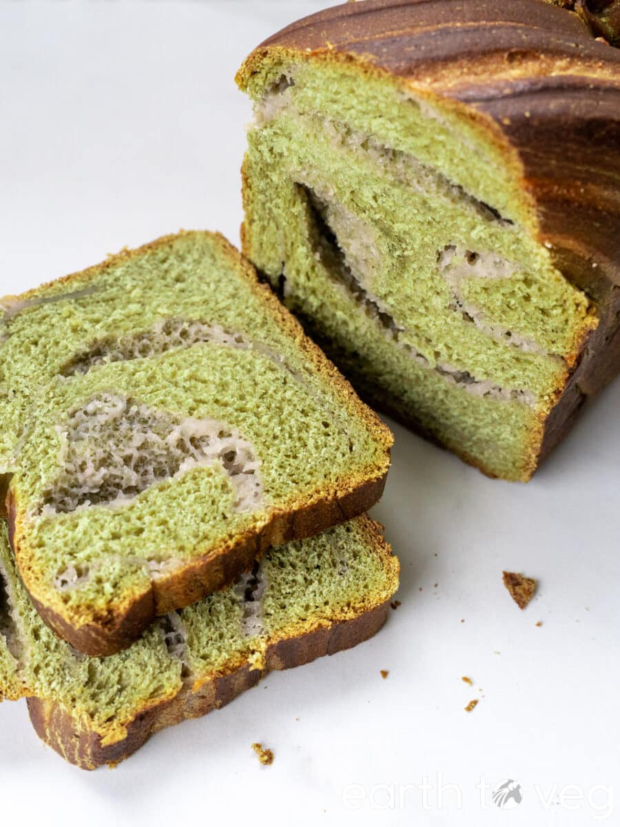A taro matcha loaf with two slices next to it reposes on a white countertop.
