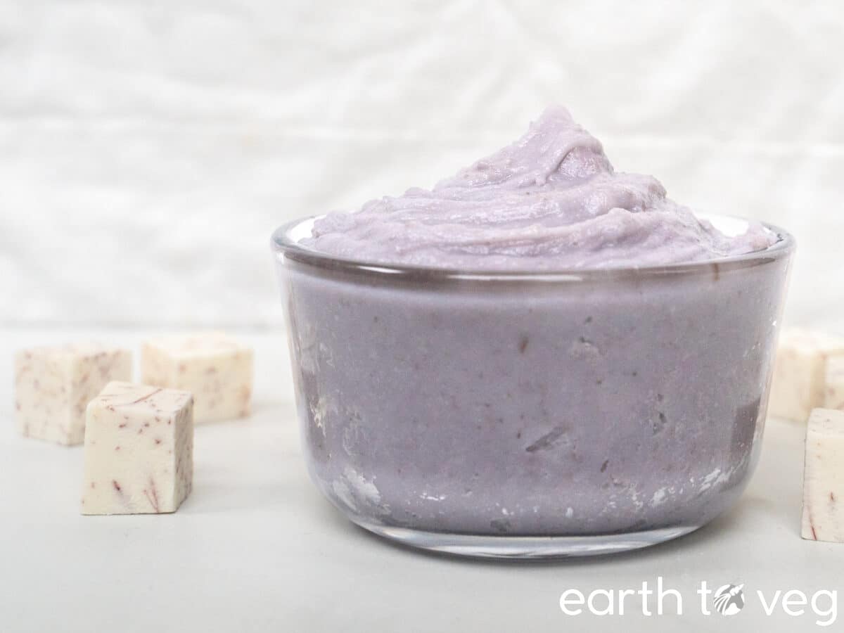 A glass container filled to the brim with blended taro paste sits on a white countertop.