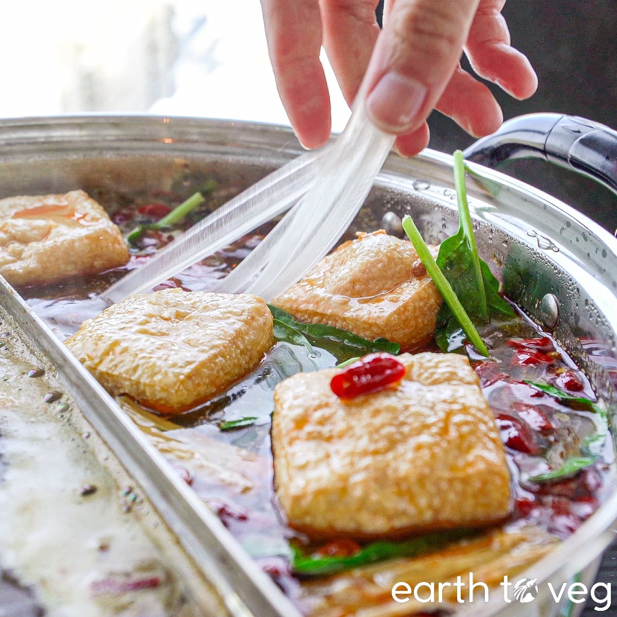 Glass noodles are added to a simmering hot pot full of vegan ingredients.