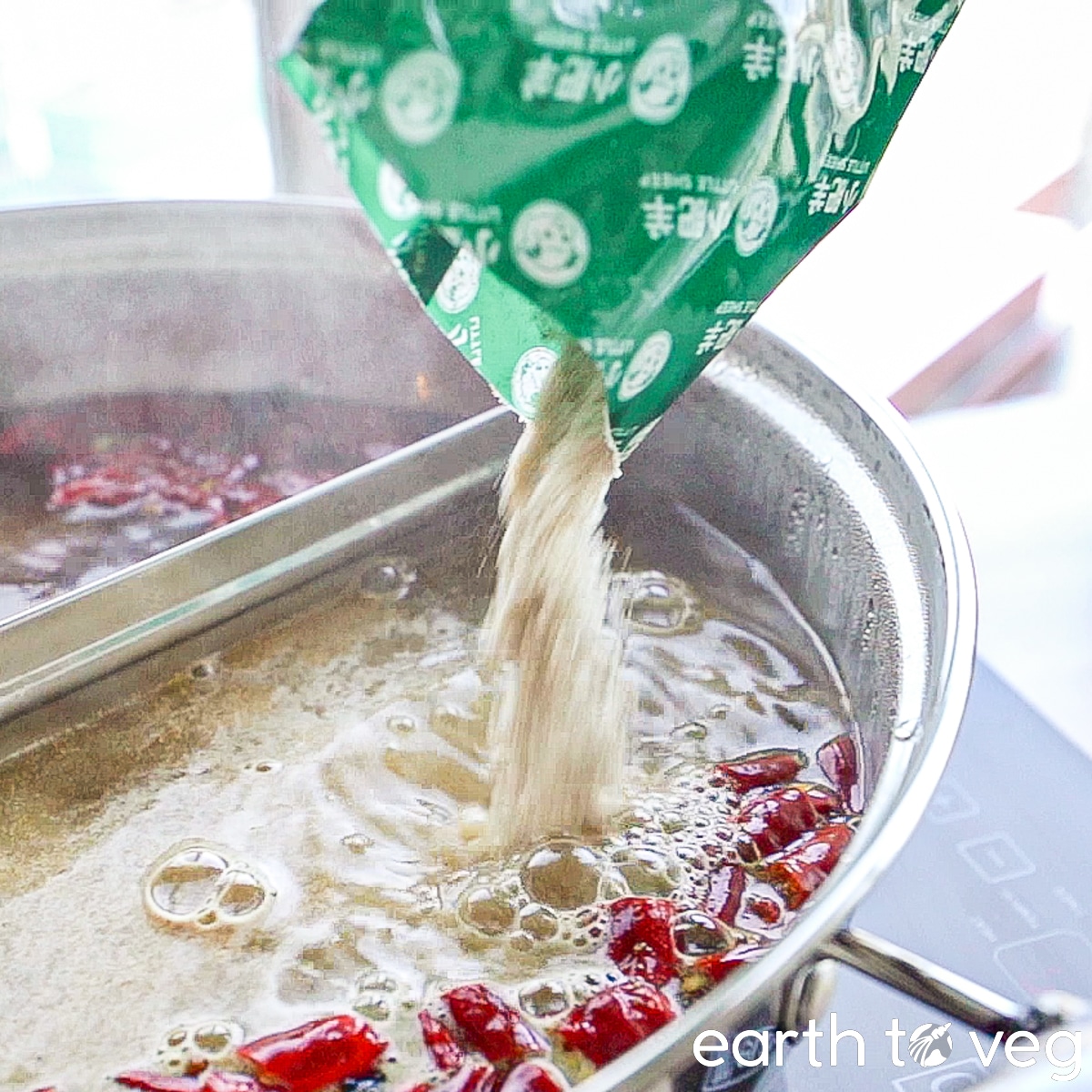 Little Lamb Hot Pot Soup Base is poured into a simmering pot of boiling water and chili peppers.
