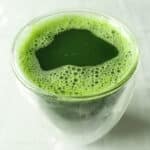 A glass cup full of pandan juice sits on a white tablecloth.