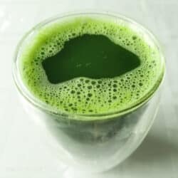 A glass cup full of pandan juice sits on a white tablecloth.