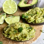 Two avocado halves are filled with guacamole, with limes in the background.
