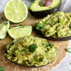 Two avocado halves are filled with guacamole, with limes in the background.
