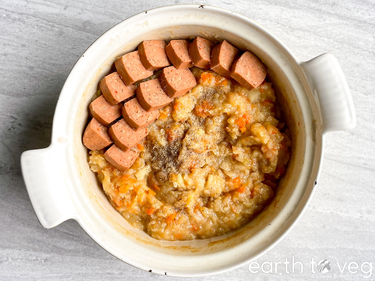 A Dutch oven full of hutspot with sausage on a grey tabletop.