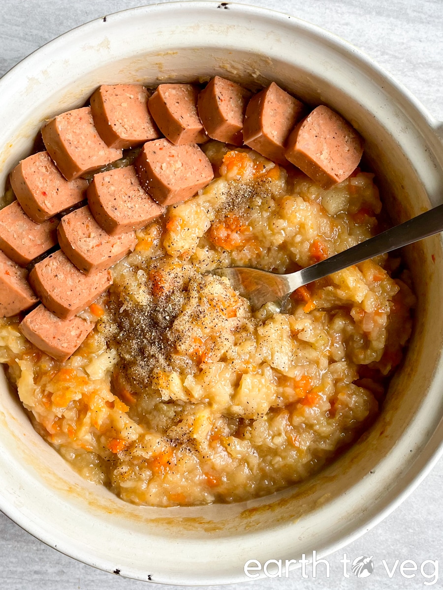 Dutch oven filled with vegan hutspot with yves veggie sausage, with spoon lying on top.