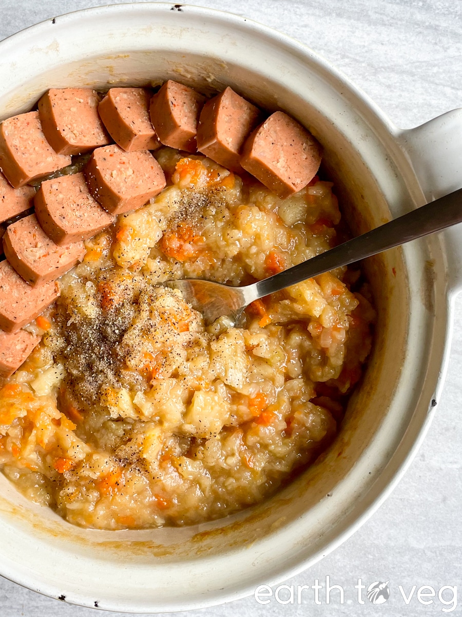Metal spoon scooping from a Dutch oven full of hutspot mashed vegetables and sausage.
