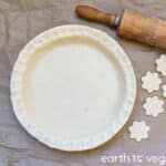 unbaked pie crust with rolling pin and flower-shaped crust cut outs on the side