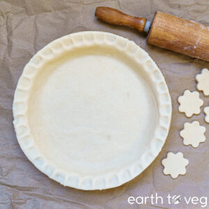 unbaked pie crust with rolling pin and flower-shaped crust cut outs on the side
