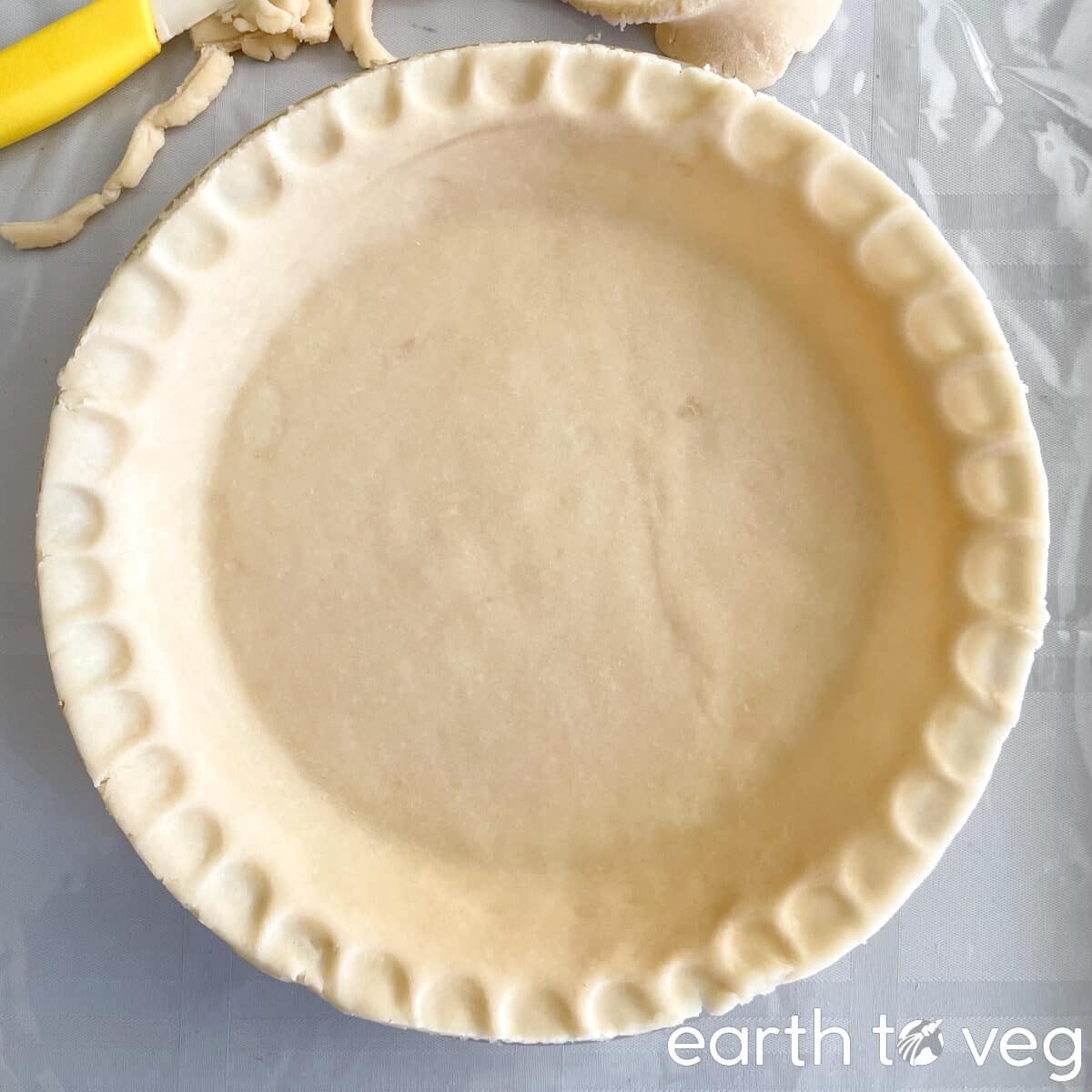 Unbaked pie crust with spare pastry crust cuttings in the background.