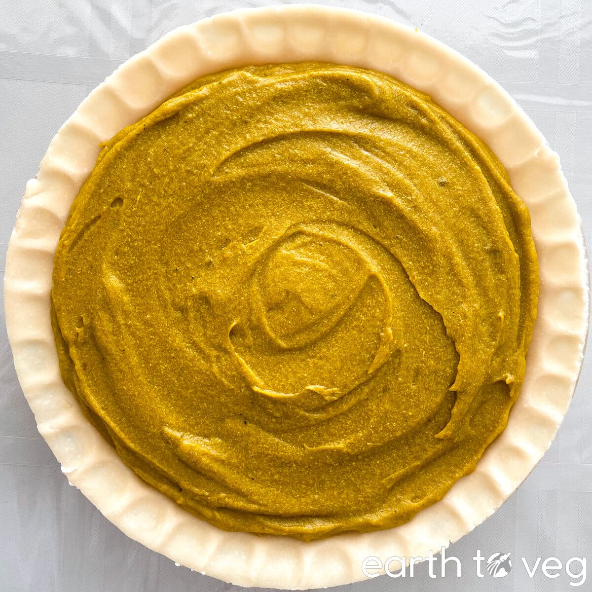 A filled unbaked pumpkin pie on a white tabletop.