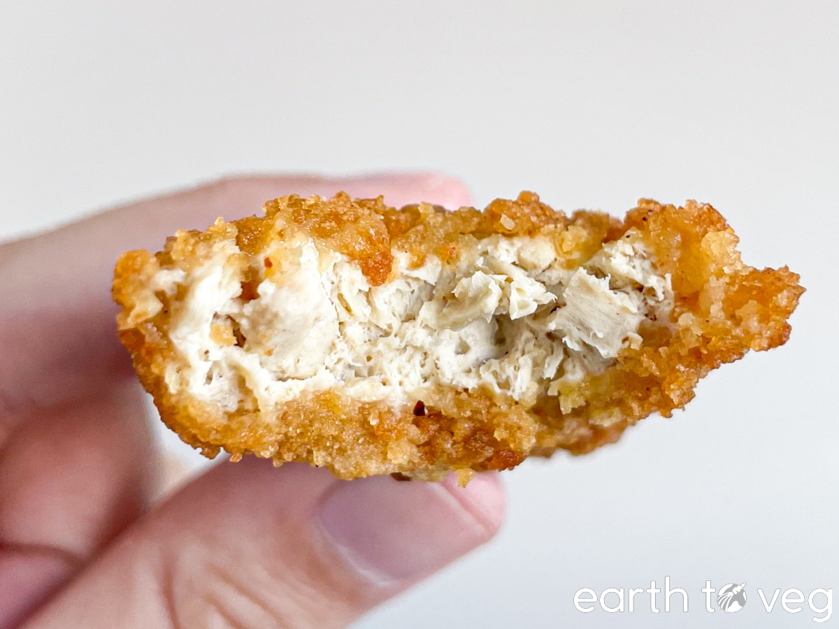 A hand holds up a Beyond Chicken Tender with a bite taken out of it.