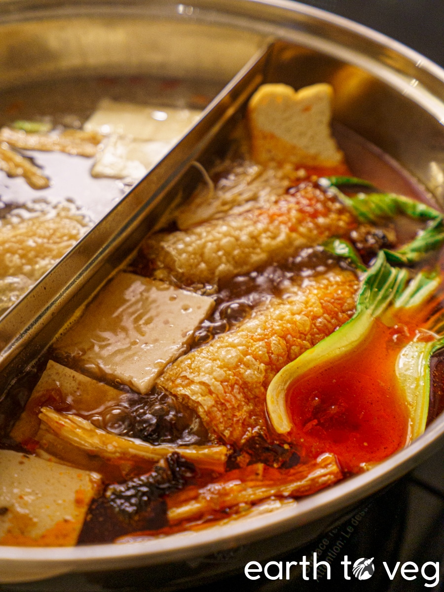 simmering spicy red chinese vegan hot pot broth filled with tofu, bok choy, soy rolls, fried bean curd, and wood ear mushrooms