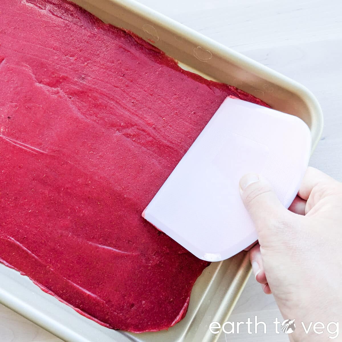 A pastry cutter smooths out hawthorn berry puree over a sheet pan.