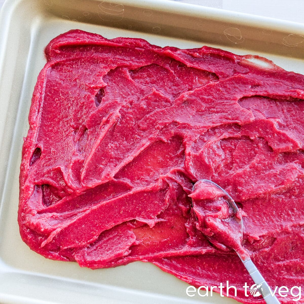 A spoon spreads hawthorn berry puree over a nonstick baking pan.