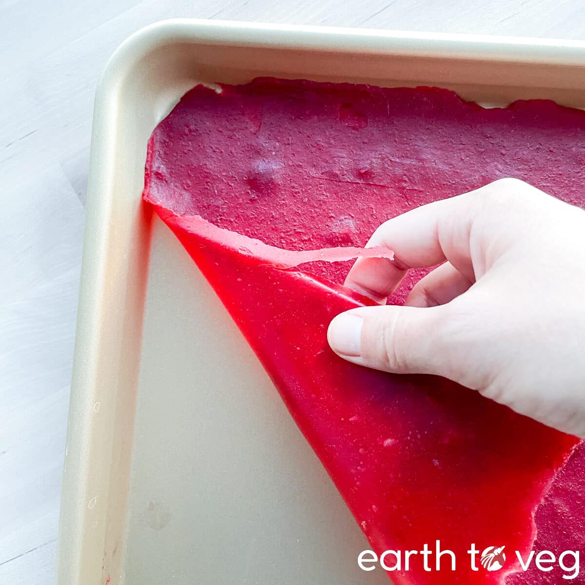 A hand peels back a layer of dried hawberry leather from a golden sheet pan.