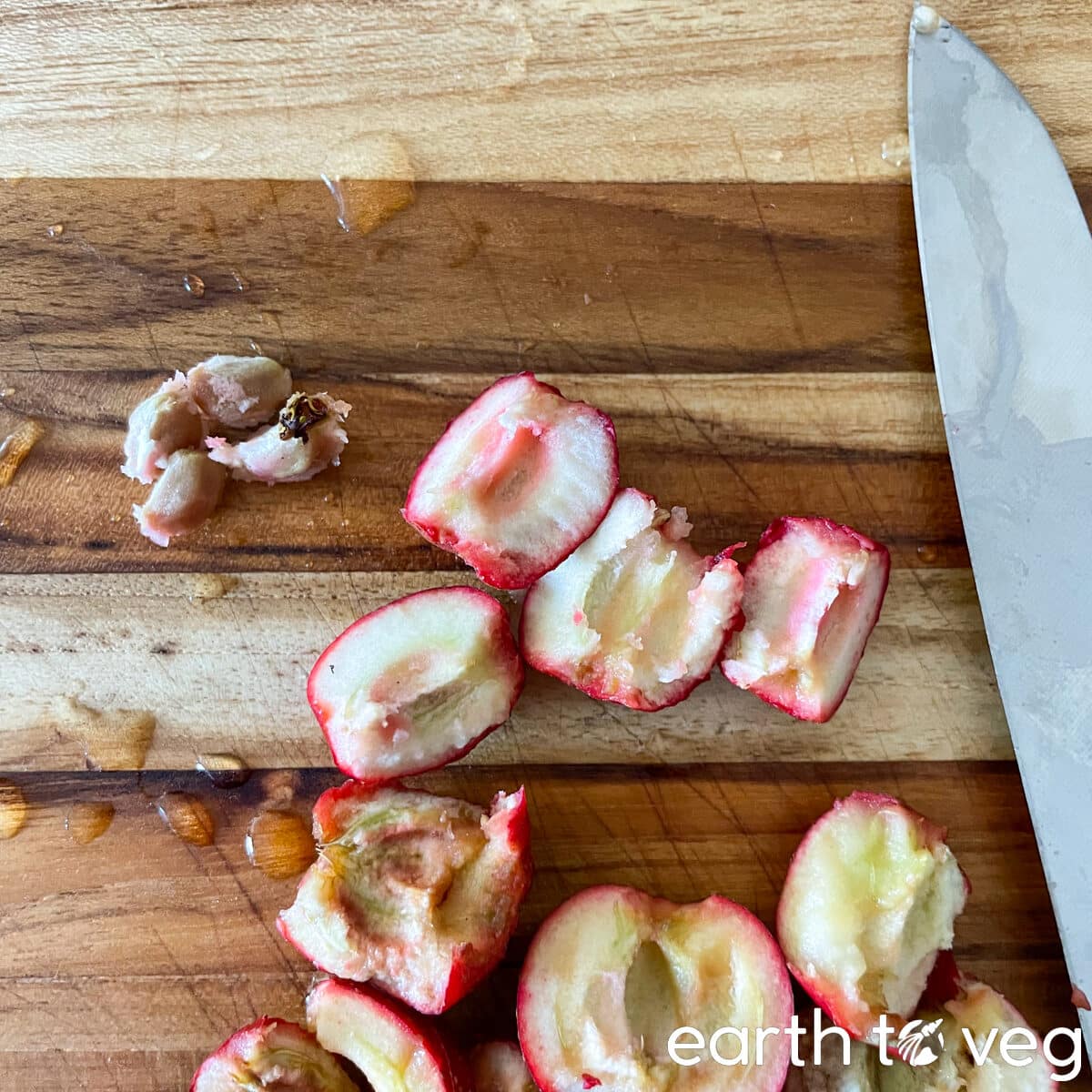 A knife resting on a wooden cutting board next to quartered and pitted hawthorn berries.