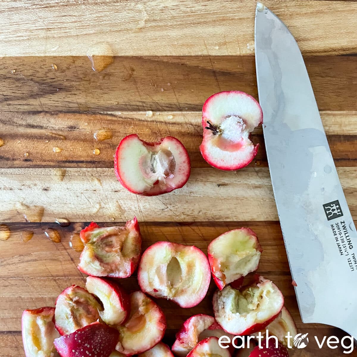 A steel knife resting on a cutting board next to split hawthorn berries.