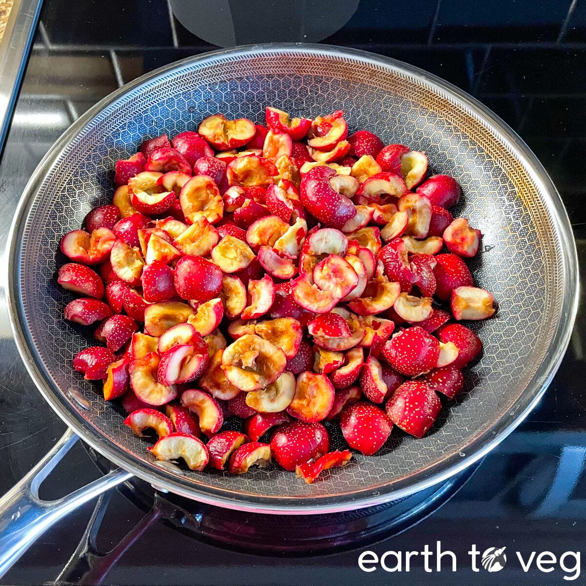 A hexclad nonstick saucepan on a black stovetop is filled with fresh Chinese hawthorn berries.